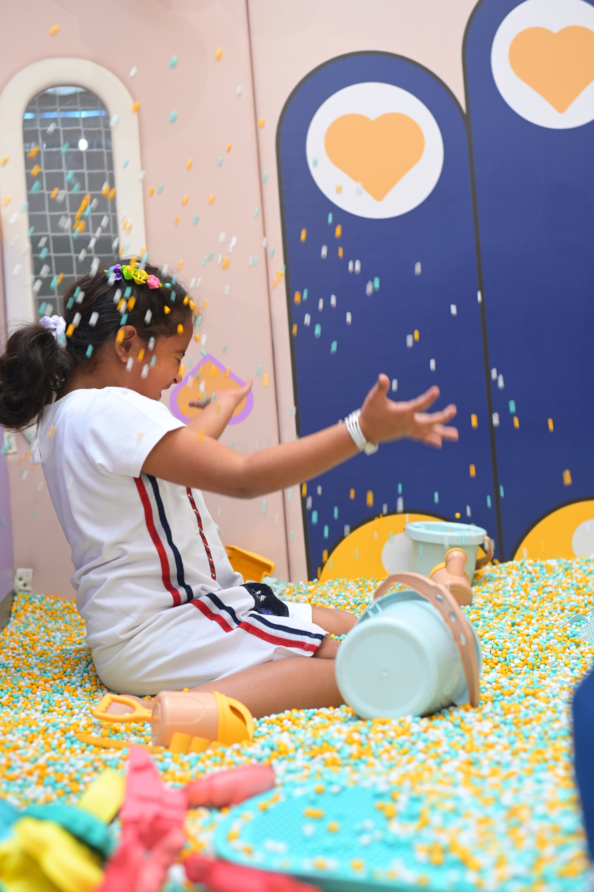 A young girl plays in a ball pit, tossing colorful balls in the air.