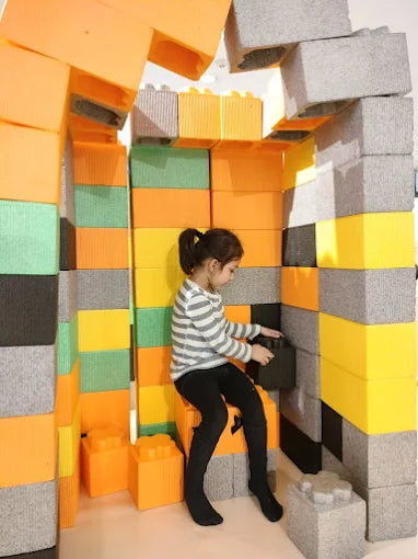 A young child plays with large foam blocks, building a colorful structure.