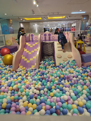 Children play in a colorful ball pit with slides and climbing structures.