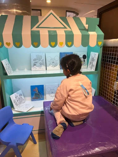 A young child sits on a purple mat in front of a colorful display of coloring pages.
