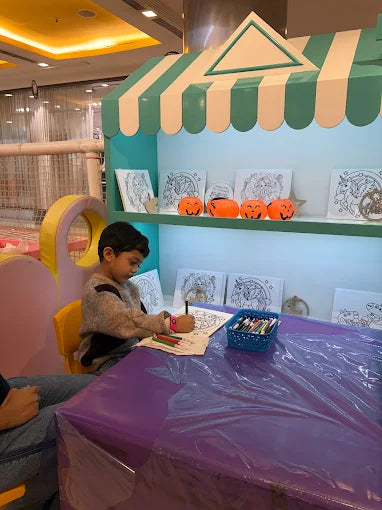 A young boy colors at a table in front of a display of Halloween-themed drawings and decorations.