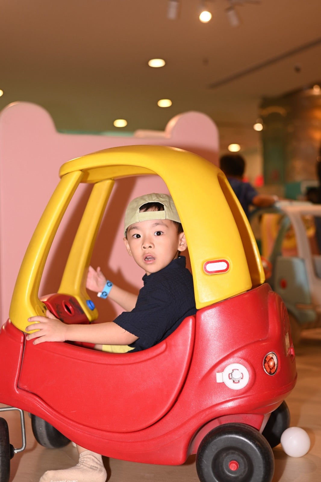 A young boy in a toy car at an indoor playground.
