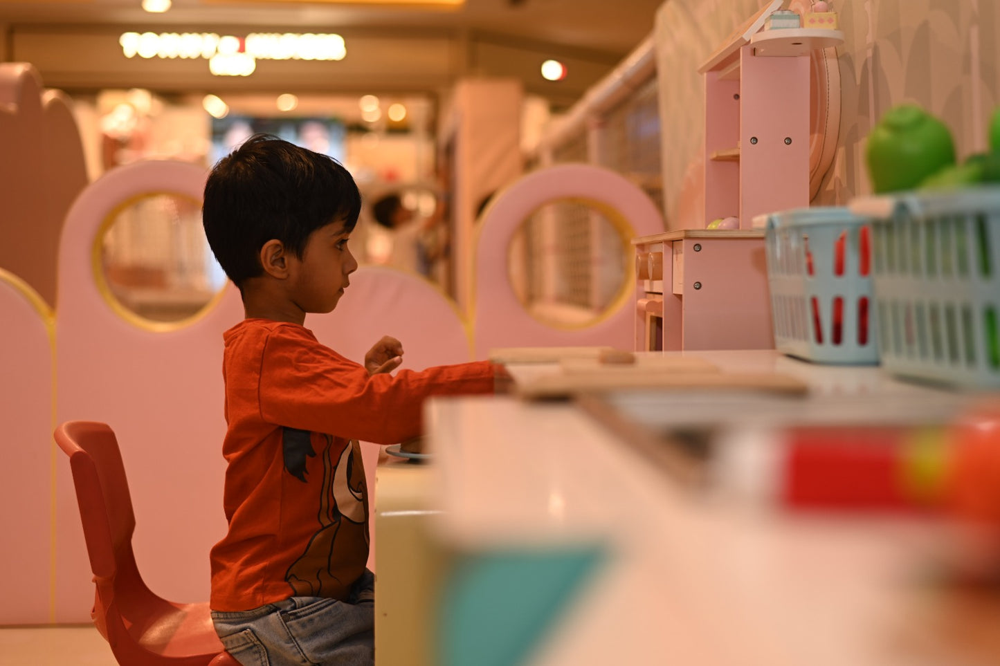 A young boy plays at a toy kitchen in a brightly colored play area.