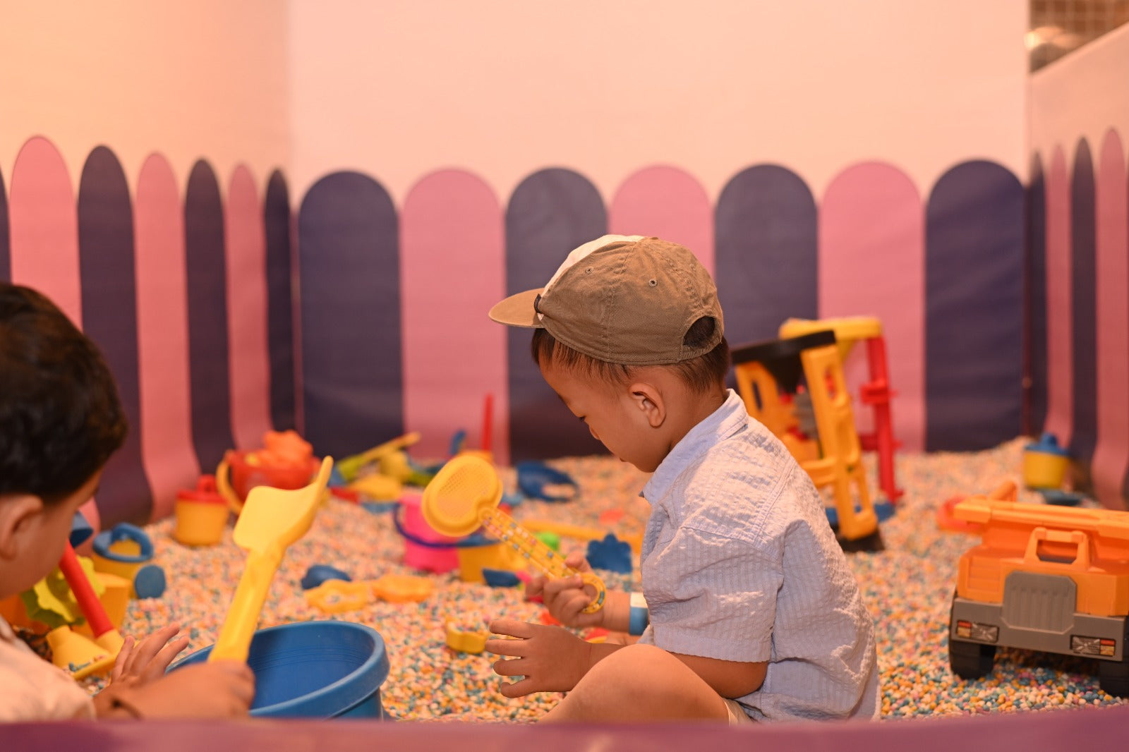 A young boy in a cap plays with sand toys in a colorful ball pit.