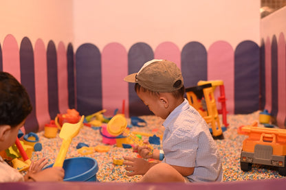 A young boy in a cap plays with sand toys in a colorful ball pit.