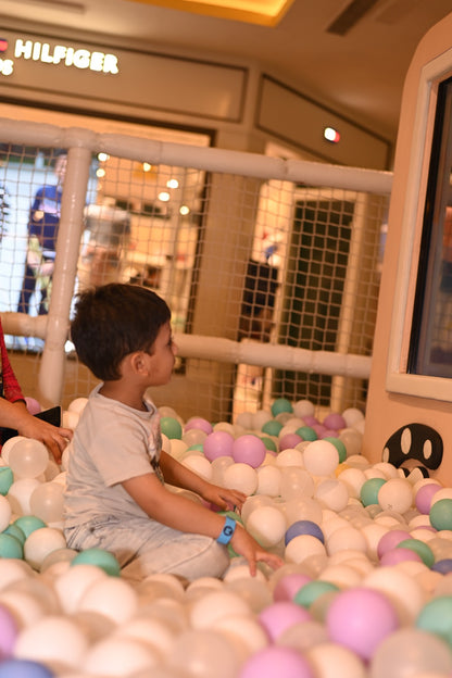 A young boy sits in a ball pit, surrounded by colorful balls, at a play area.