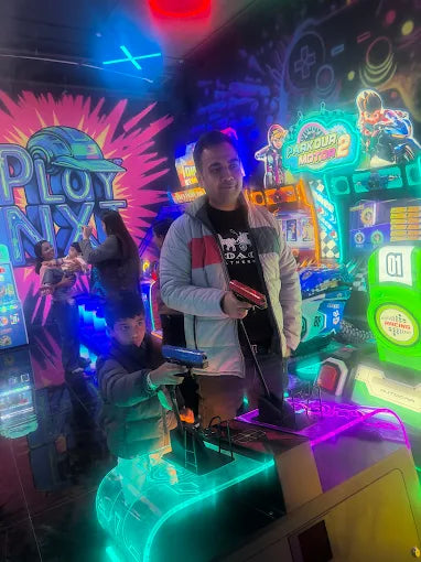A man and a boy play an arcade game with neon lights and colorful graphics.