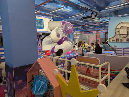 Children play in a colorful indoor playground with ball pits and slides.