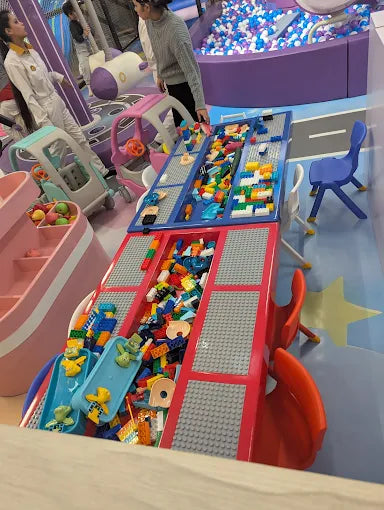 Children play with colorful building blocks and slides in a bright indoor playground.