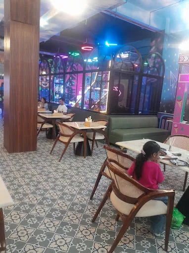 A young girl sits at a table in a brightly lit restaurant with patterned floors.