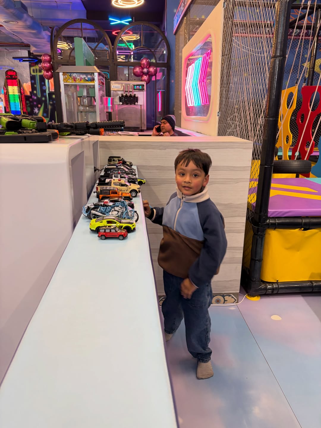 A young boy looks at toy cars displayed on a counter in an arcade.