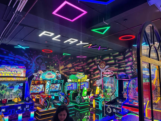 An arcade with neon lights and various games, including motorcycle racing and shooting games.