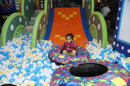 Child playing in a colorful ball pit with slides and toys in the background