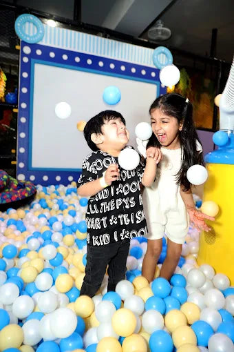 Two children playing with balloons in a ball pit at an indoor playground.