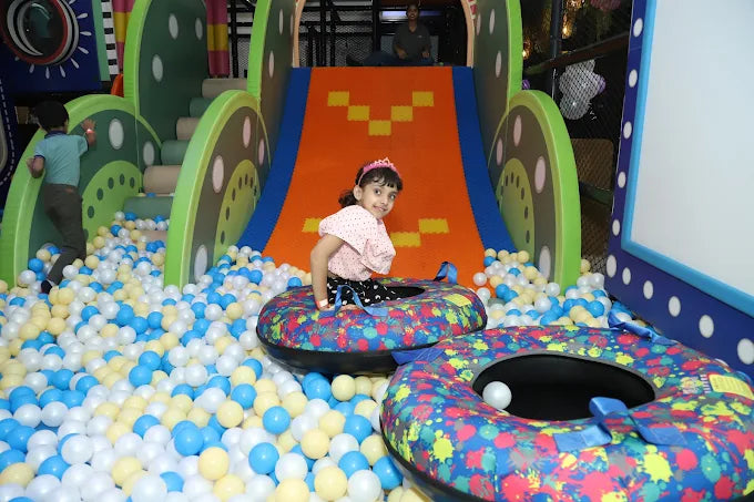 Child playing in a colorful indoor playground with slides and ball pits.