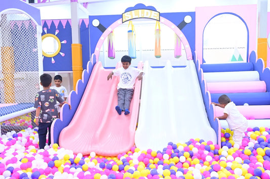 Young boys play on a colorful indoor playground with slides and a ball pit.