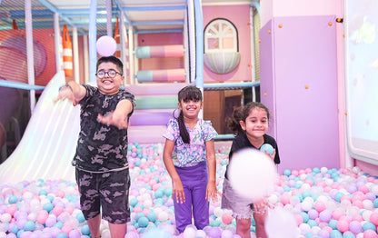 Three children play in a ball pit at an indoor playground.