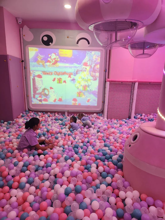 Children play in a ball pit in front of a projected Christmas scene.