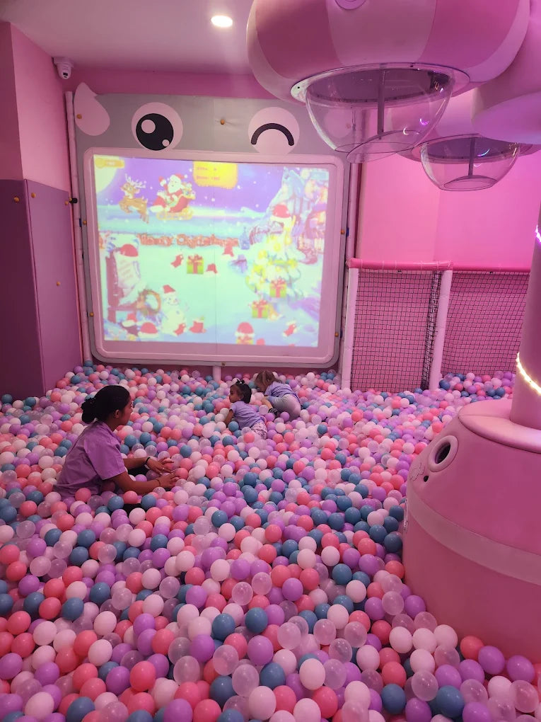 Children play in a ball pit in front of a projected Christmas scene.