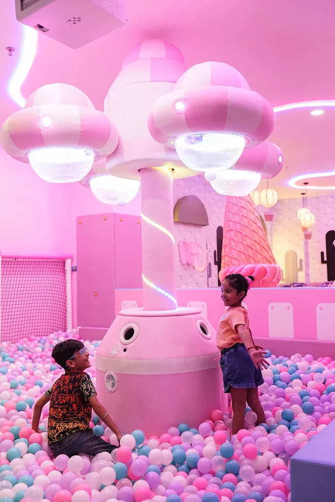 Two children play in a pink ball pit with a large, cloud-shaped structure.