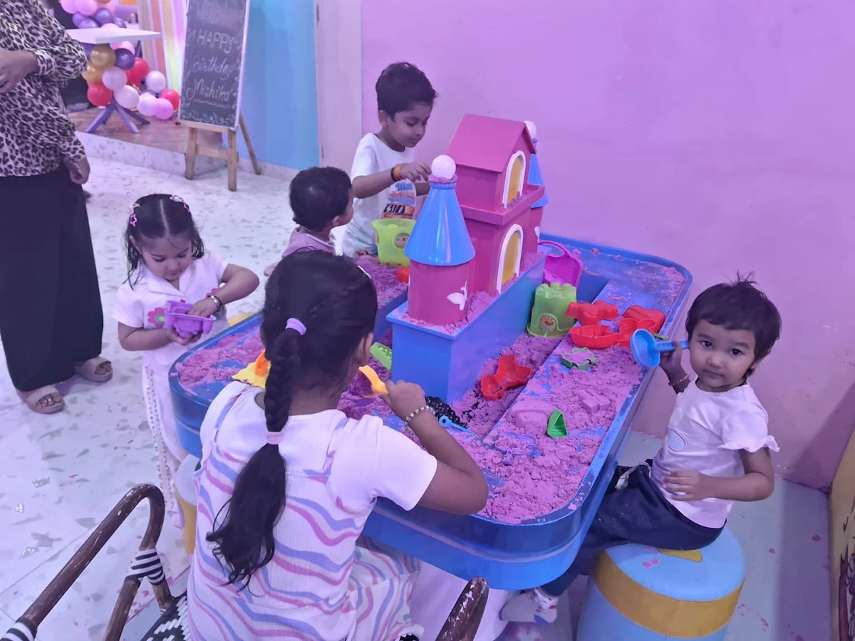 Young children play with kinetic sand and a toy castle at a birthday party.