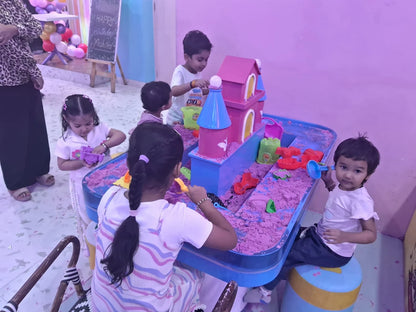 Young children play with kinetic sand and a toy castle at a birthday party.