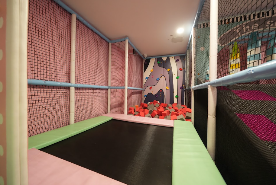 A trampoline with a foam pit and climbing wall in a children's play area.