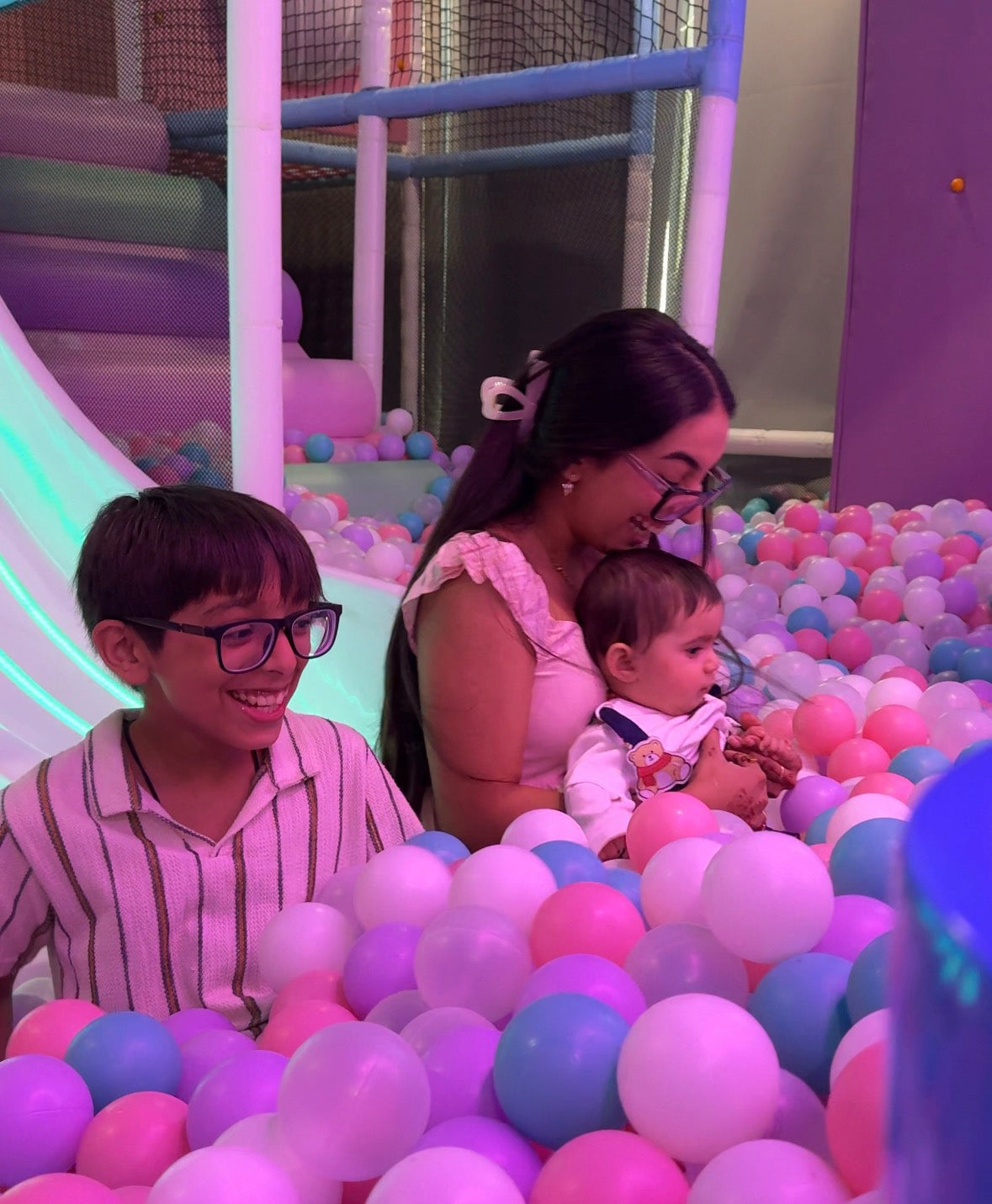 A young boy and a woman holding a baby in a colorful ball pit.
