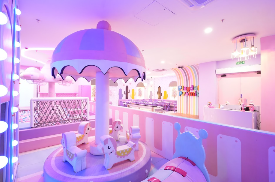 A brightly lit pink and purple indoor playground with a carousel and ball pit for children.