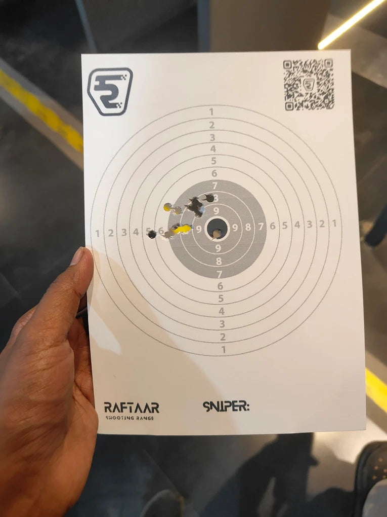 A person holds a target with bullet holes from a shooting range.