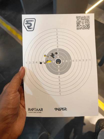 A person holds a target with bullet holes from a shooting range.