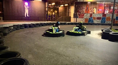 Two go-karts with drivers race on a track at night, with a neon astronaut figure visible in the background.