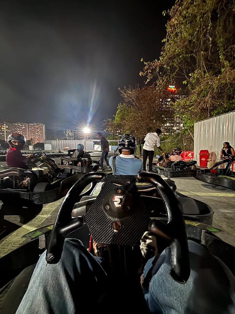People in go-karts at a nighttime track, with city lights in the background.