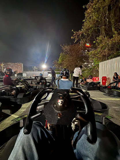People in go-karts at a nighttime track, with city lights in the background.