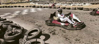 A young person in a helmet drives a go-kart on a track lined with tires.