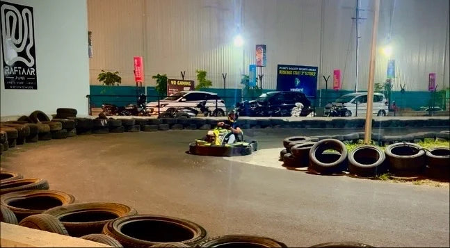 A person races a go-kart on a track at night, with cars and tires lining the course.