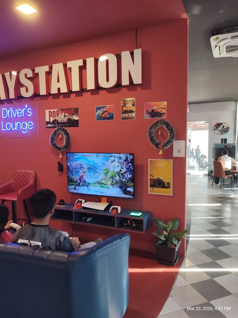 Young people play video games in a brightly lit lounge with "Playstation" signage and car-themed decor.