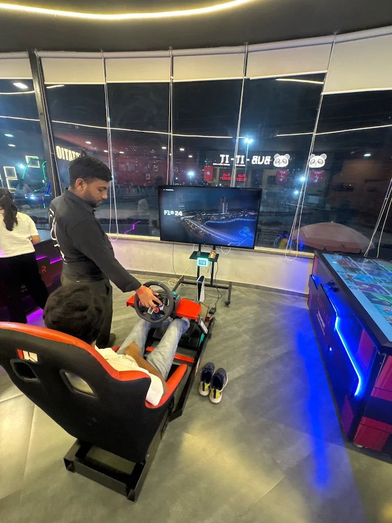 A young person plays a racing simulator game while another person stands nearby.