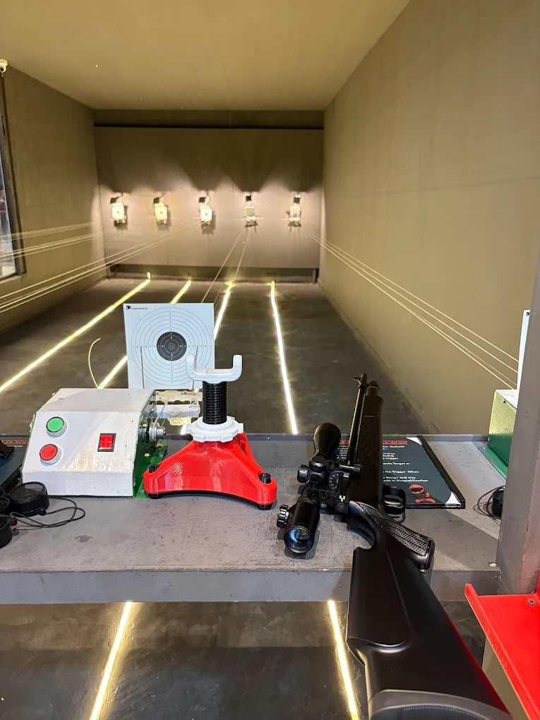A rifle with a scope rests on a table in a shooting range, with targets visible in the distance.