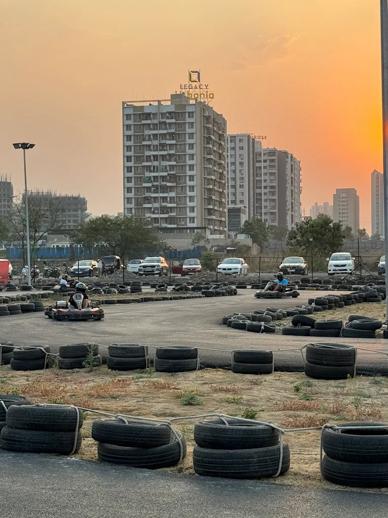 Go-karts race on a track with tires as barriers, with apartment buildings in the background at sunset.