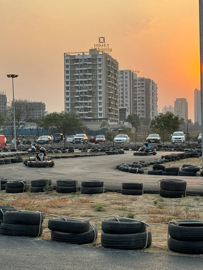 Go-karts race on a track with tires as barriers, with apartment buildings in the background at sunset.