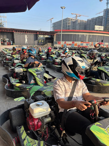 Adults in helmets race go-karts on a track with construction in the background.