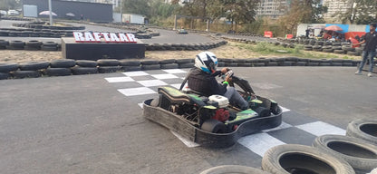 A person in a helmet races a go-kart on a track lined with tires, with a sign that reads "RAFTAAR."