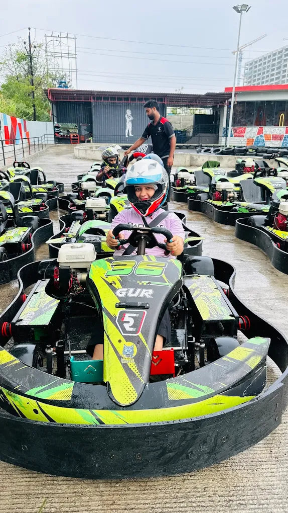 A young person in a go-kart helmet smiles while sitting in a go-kart, ready to race.