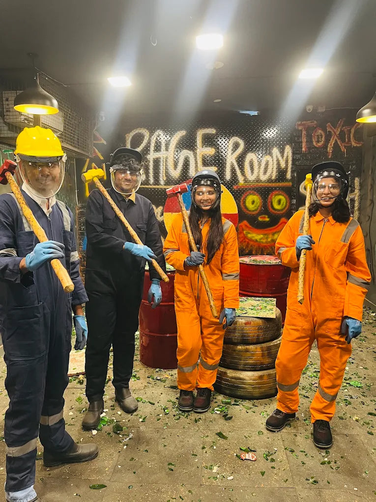 Four young adults in protective gear hold mallets in a room filled with broken glass.