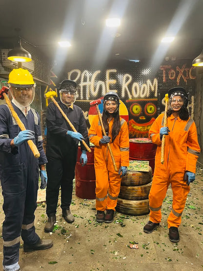 Four young adults in protective gear hold mallets in a room filled with broken glass.