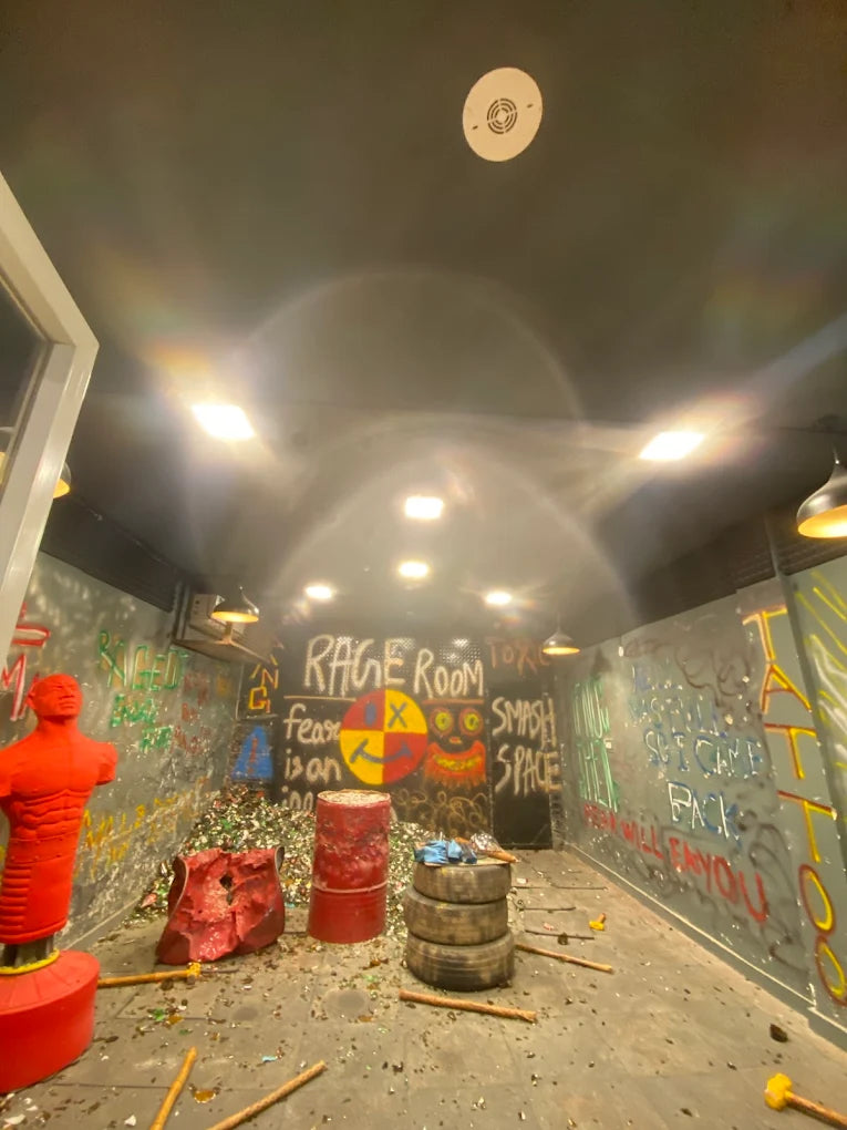 A rage room with broken glass, tires, and graffiti, featuring a red punching dummy.