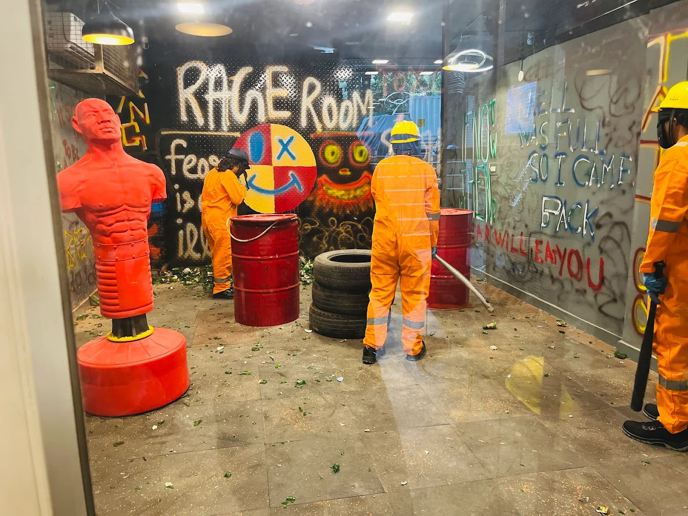 Adults in orange jumpsuits smash bottles in a graffiti-covered rage room.