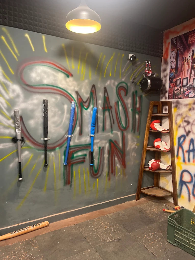 A room with graffiti that says "SMASH FUN," baseball bats, and boxing gloves on a shelf.