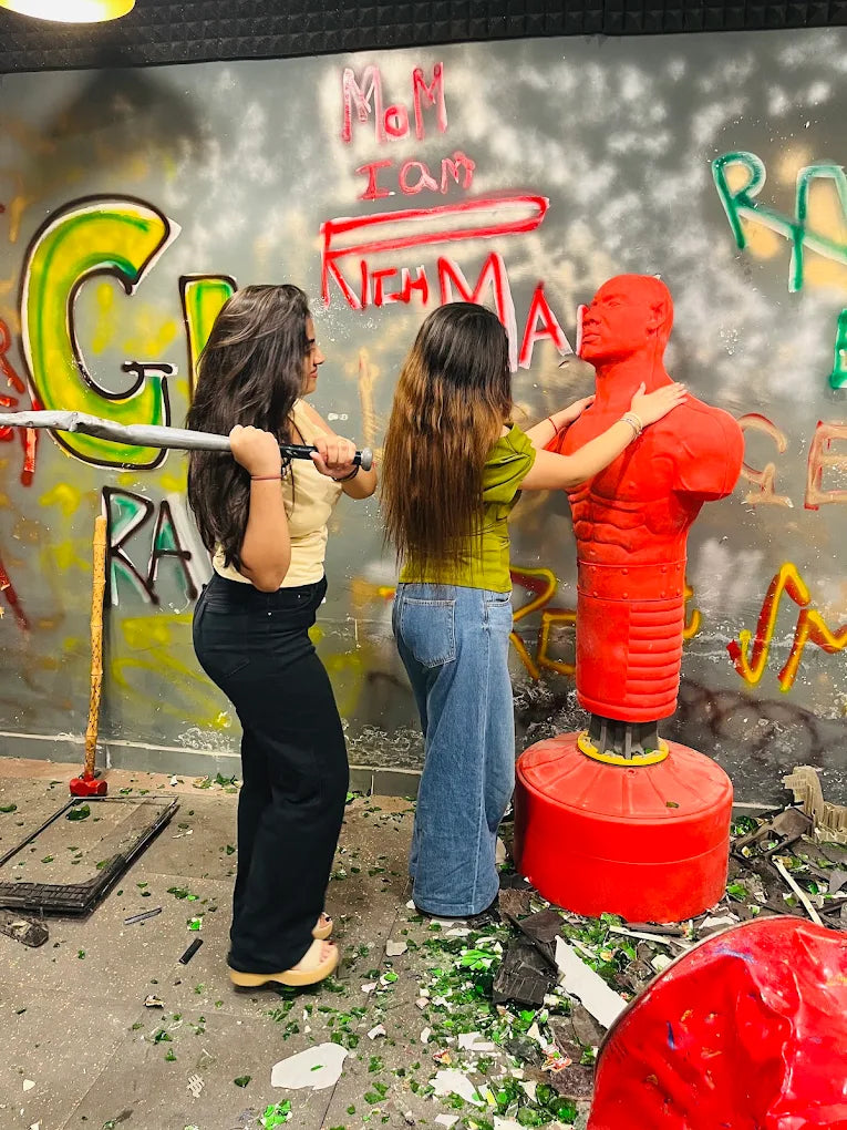 Two young women in a graffiti-covered room with a red punching dummy, one holding a metal bar.